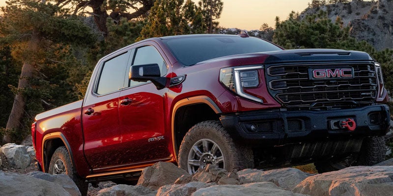 Red 2026 GMC Sierra 1500 parked on boulders in open forested area